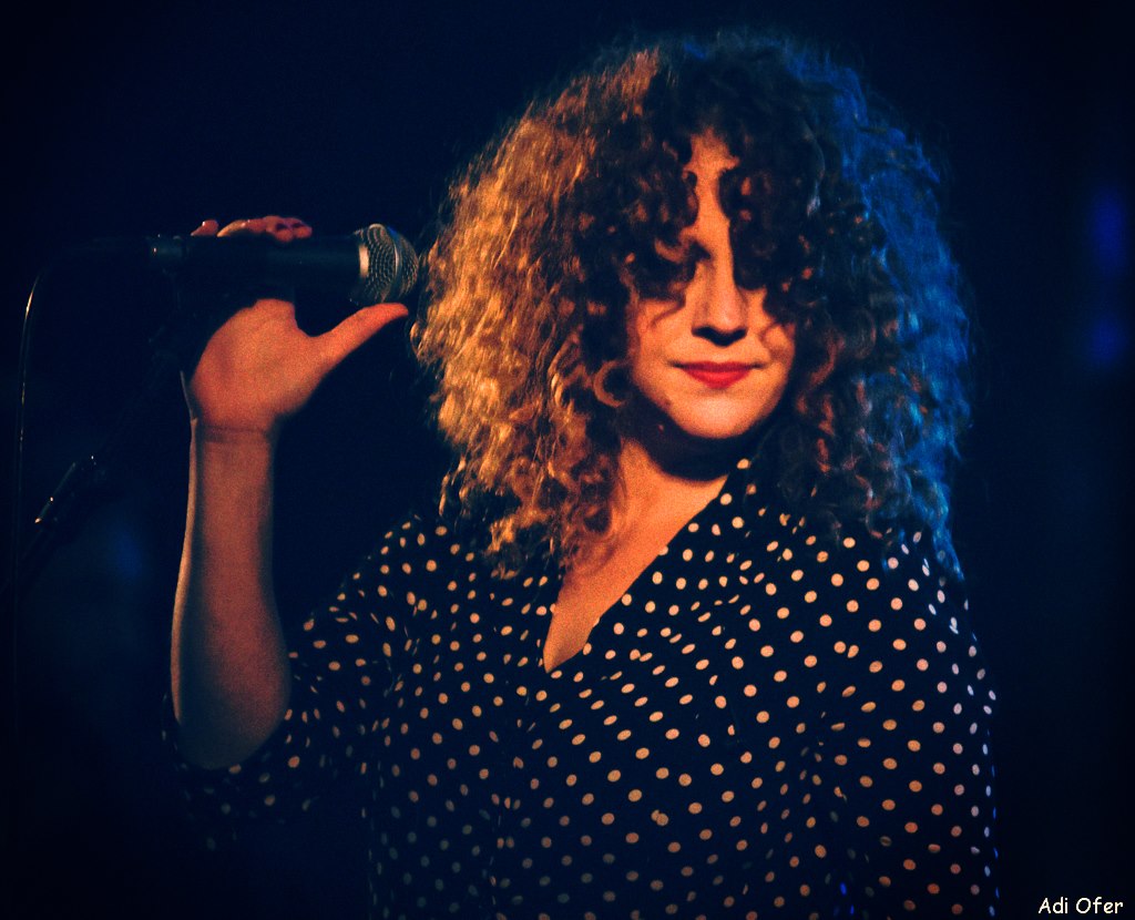 Noa holding a microphone in warm amber and blue light