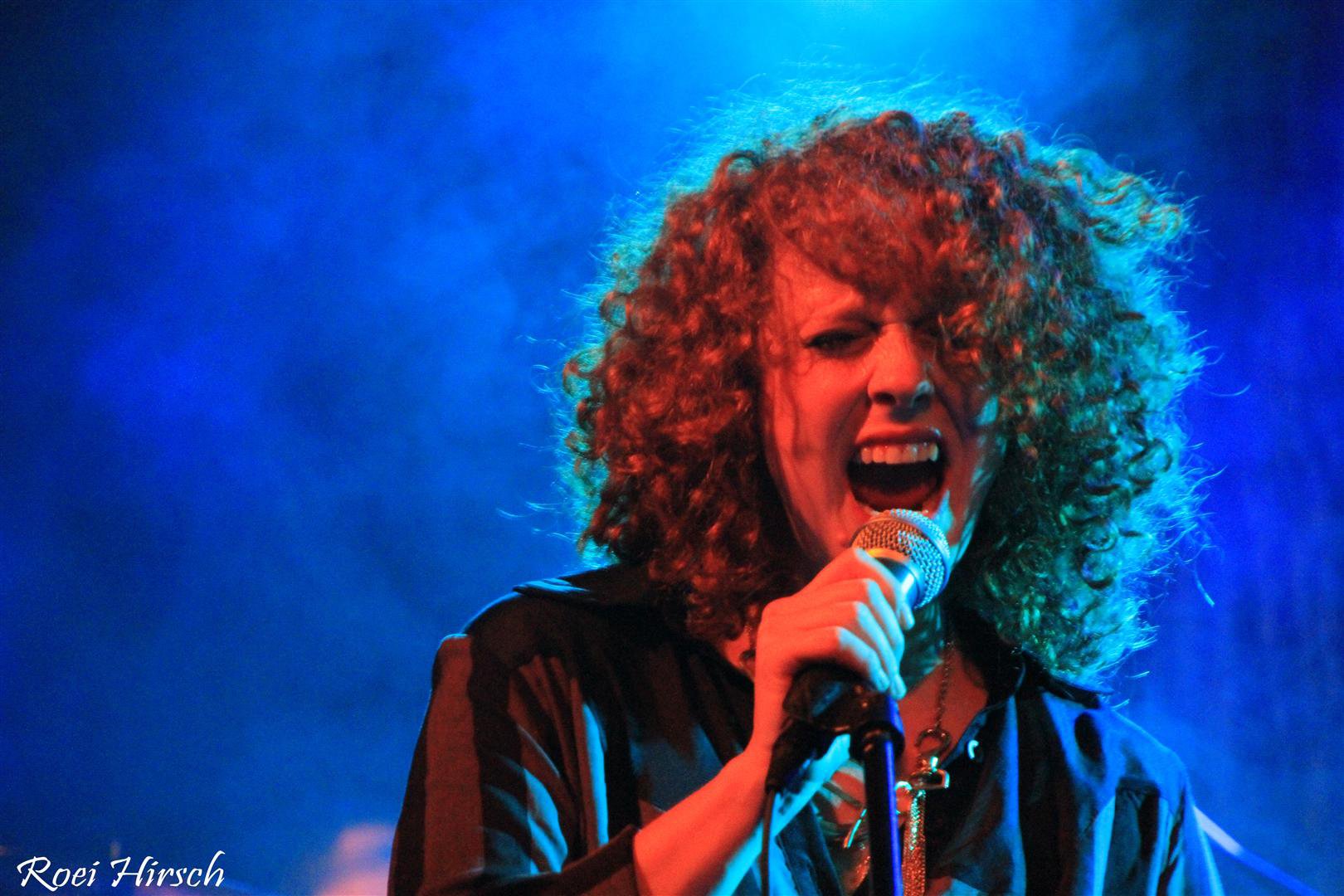 Noa singing under electric blue and red stage lights