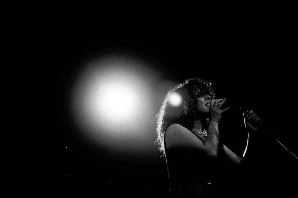 Noa Lembersky singing on a dark stage under bright spotlights